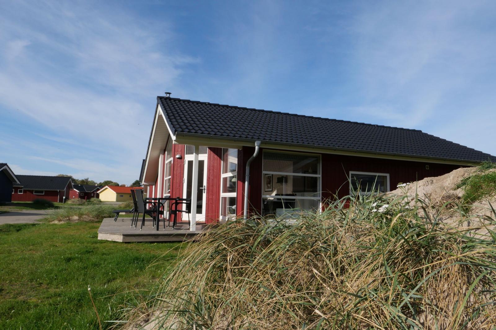 Rotes Ferienhaus mit Terrasse und Garten. Sicht auf Wohnbereich durch große Fenster.