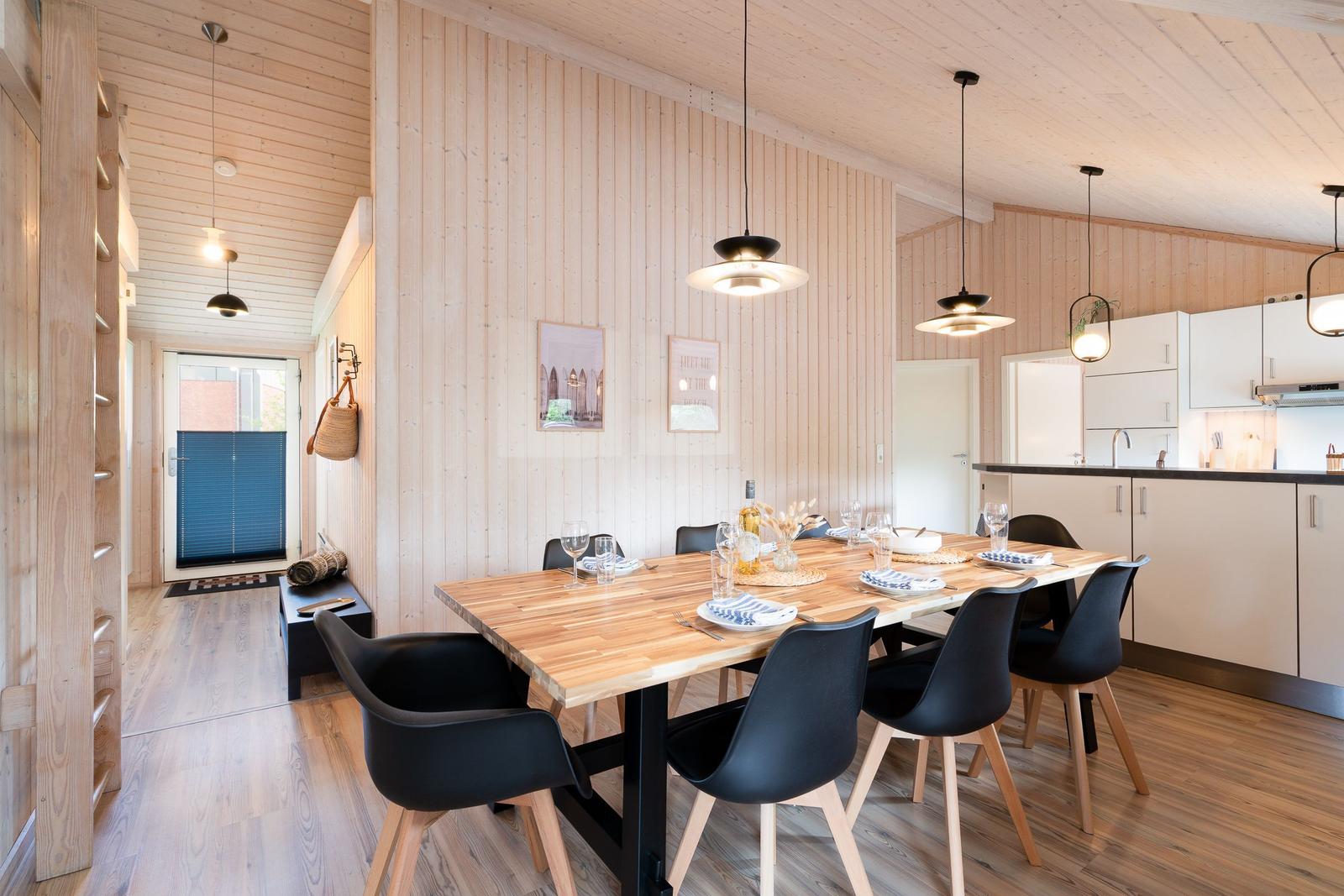 Essbereich mit Holztisch, schwarzen Stühlen und Küchenzeile im Hintergrund.