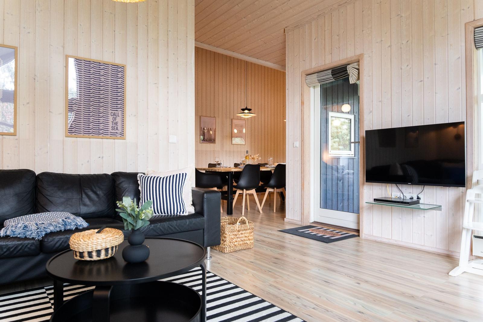 Wohnzimmer mit Sofa, Couchtisch und Fernseher. Im Hintergrund Essbereich mit Tisch und Stühlen.