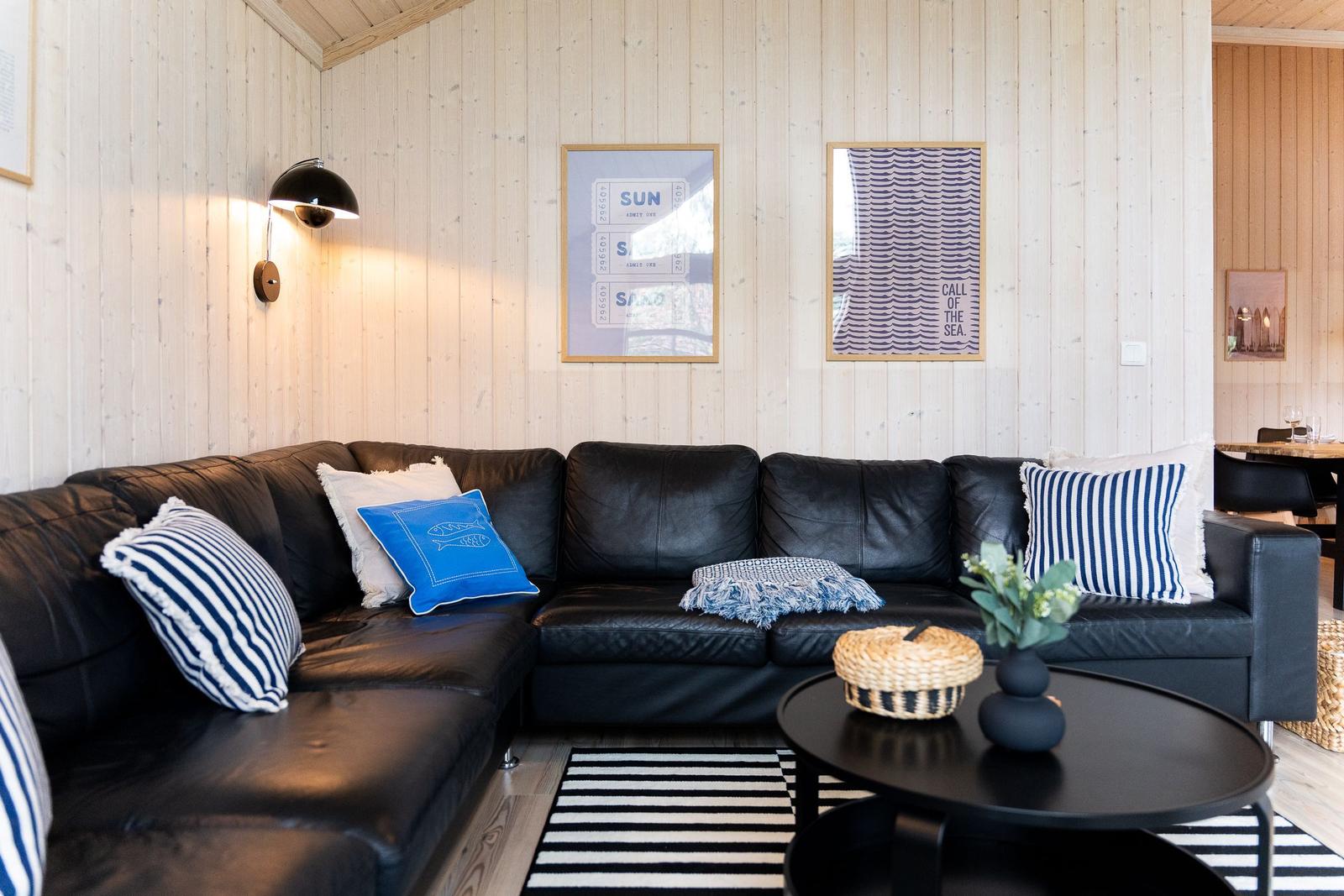 Schwarzes Ledersofa mit Kissen, Wandbilder und runder Tisch im Wohnzimmer.