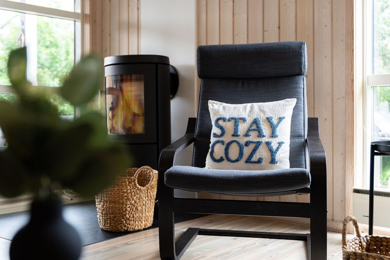 Schwarze Sessel mit Kissen STAY COZY vor Kamin und Holzwand.