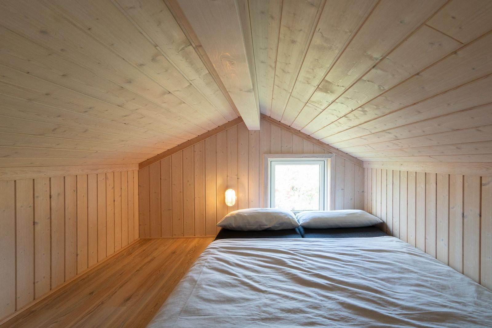 Schlafzimmer mit Holzwand und -decke, Bett mit weißen Kissen und Fenster.