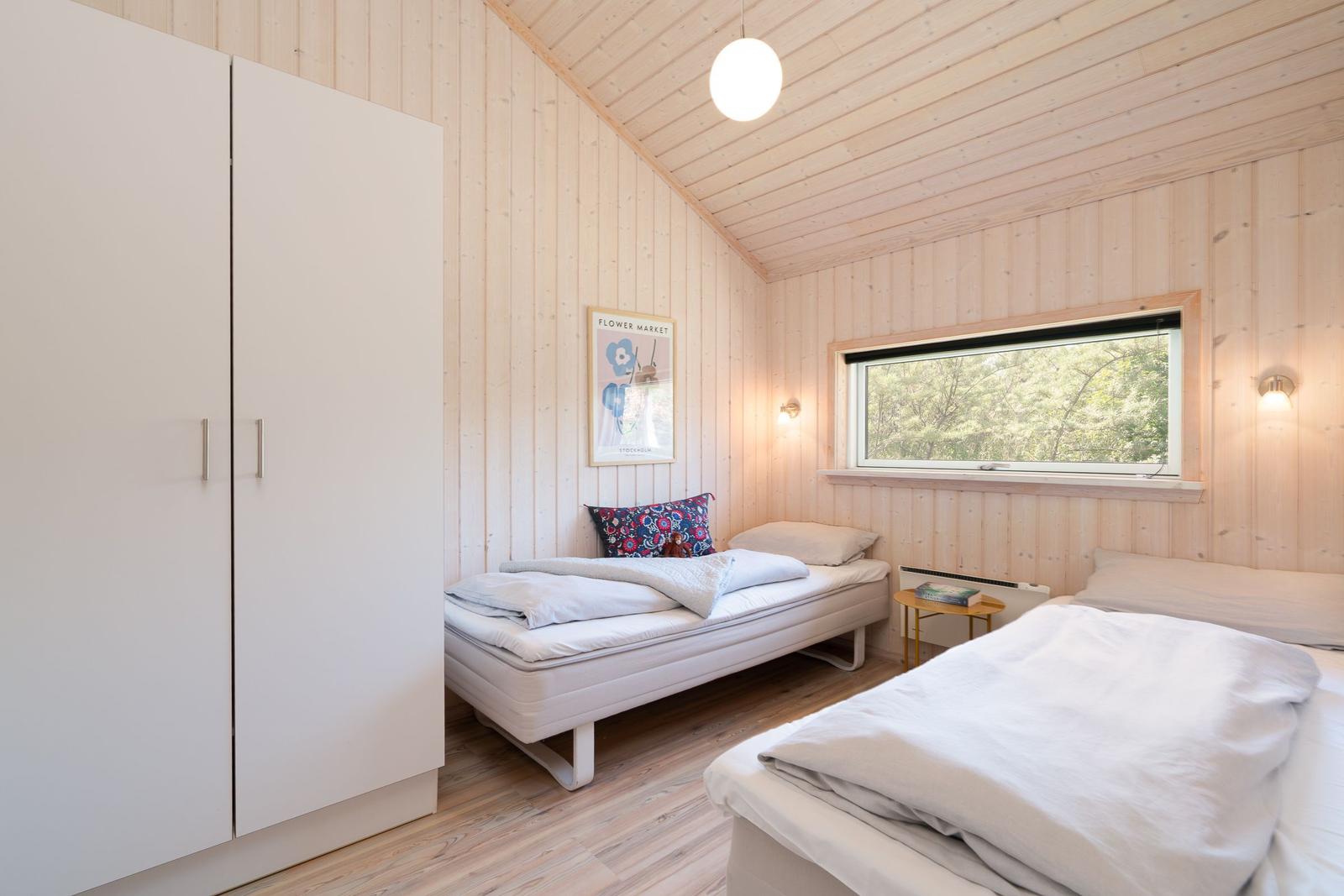 Zimmer mit zwei Betten, Kleiderschrank und Fenster mit Blick auf Wald.