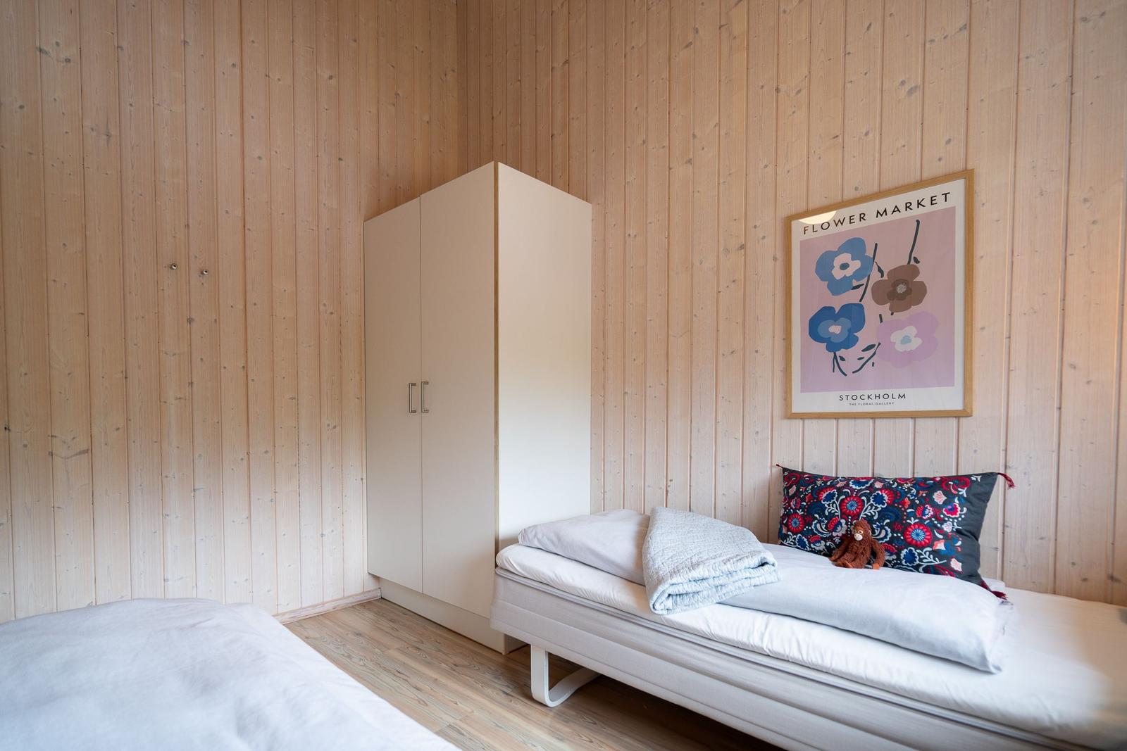 Schlafzimmer mit Holzwand, Bett, Kleiderschrank und Poster an der Wand.