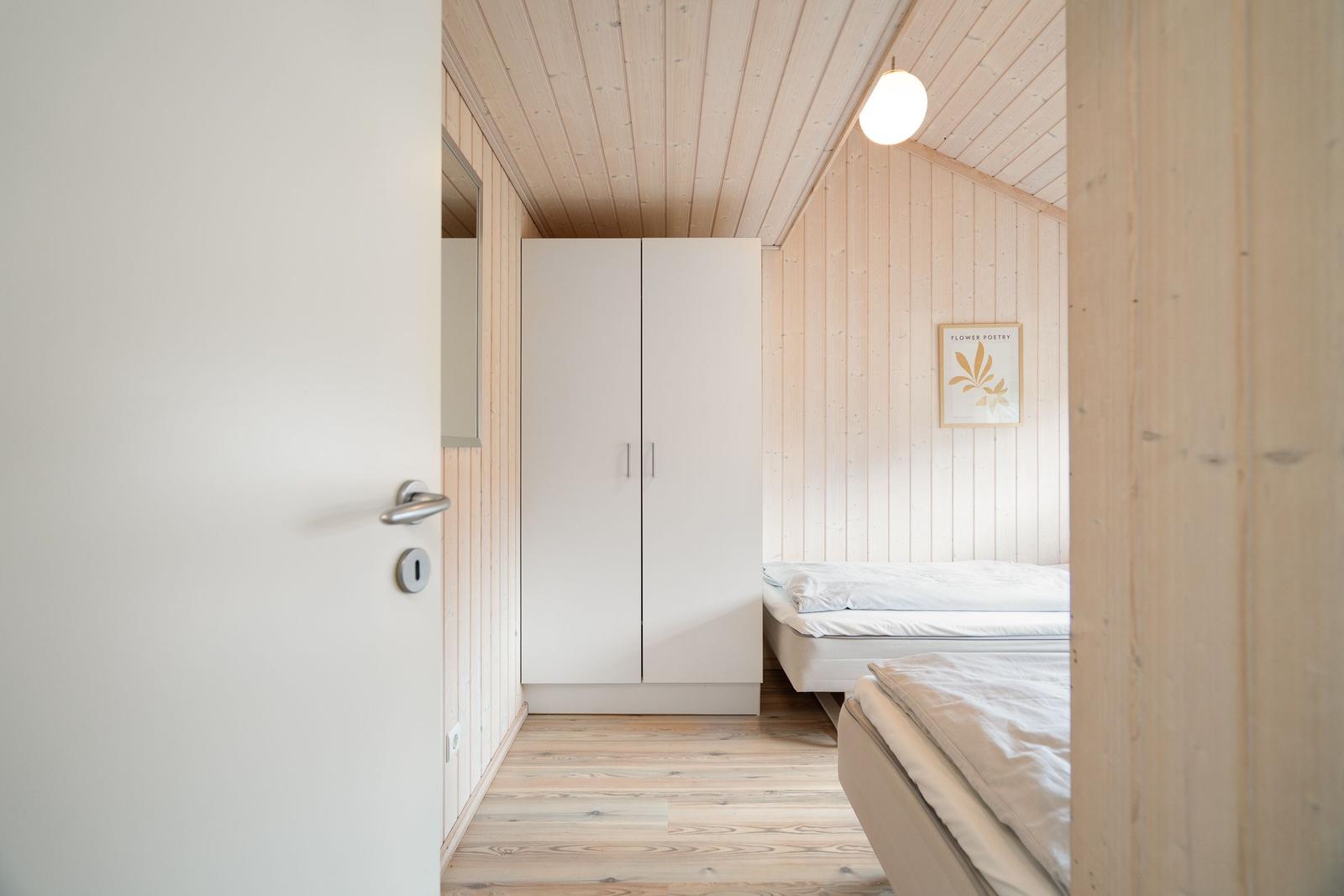 Zimmer mit zwei Betten, weißen Schränken und Holzwandverkleidung.