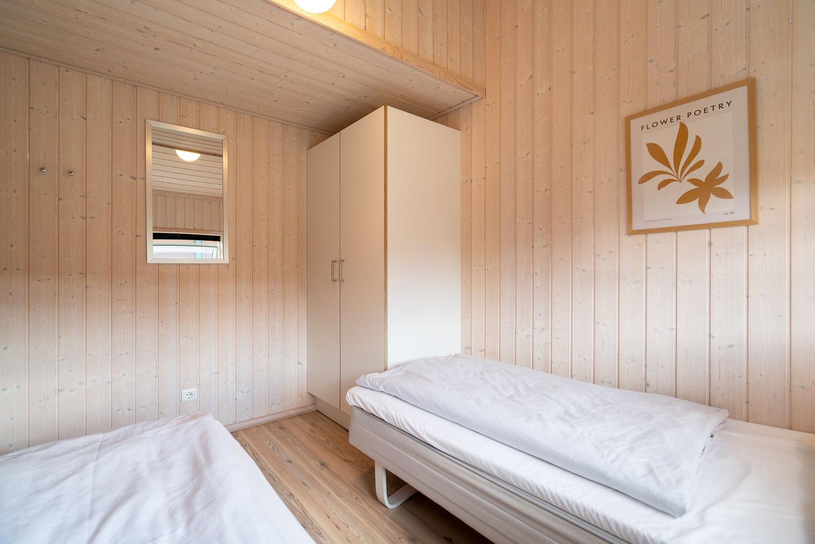 Zimmer mit zwei Betten, Holzwand und Kleiderschrank. Wandbild und Spiegel sichtbar.