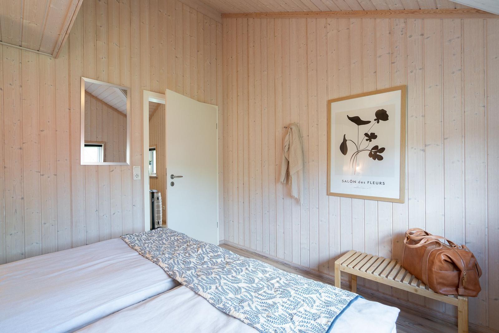 Schlafzimmer mit Holzwand, Bett, Bild und Bänkchen mit Tasche.
