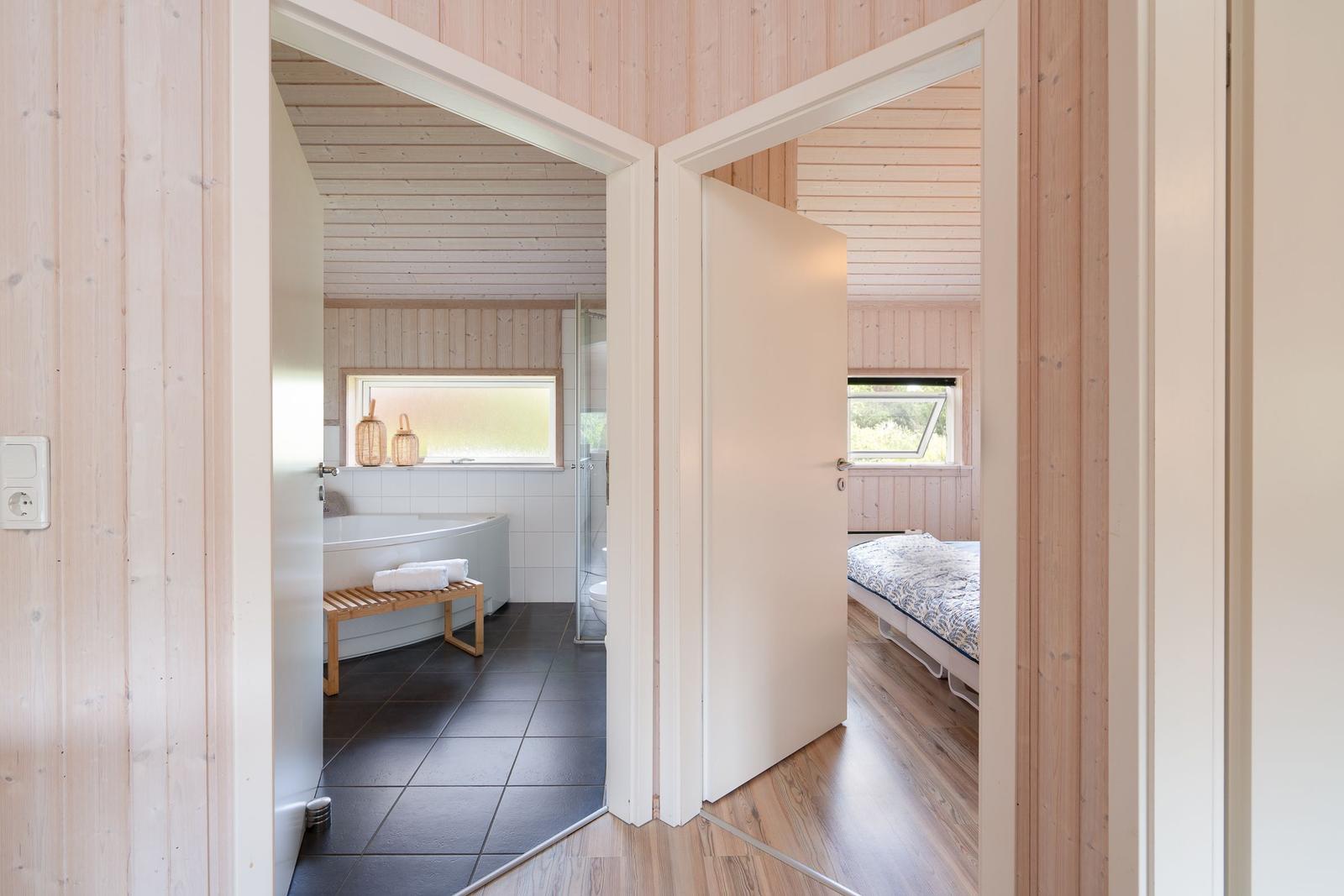 Badezimmer mit Badewanne und Dusche. Nebenraum mit Bett und Fenster.