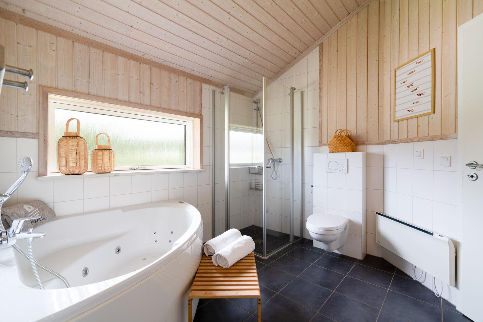 Bad mit Whirlpool, Dusche und Toilette. Holzwände und Fenster mit Wickerkörben.