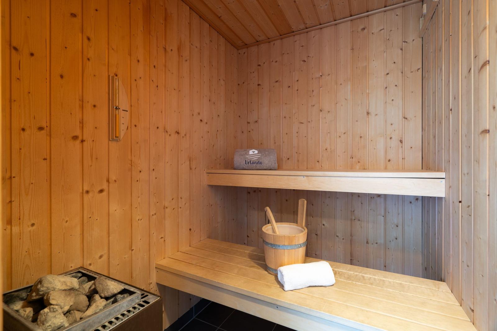 Sauna mit Holzwand, Sitzbank, Korb und Handtuch.