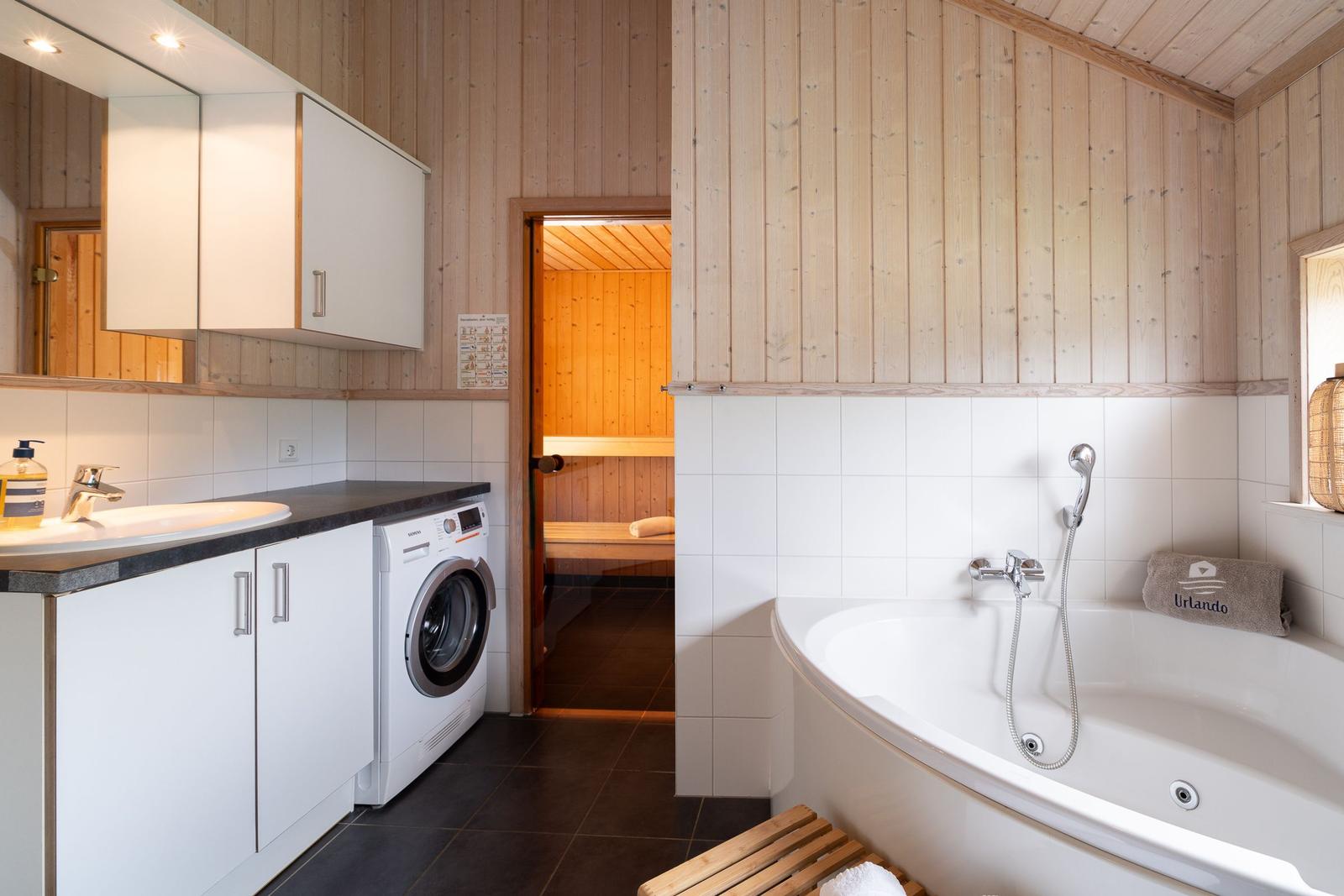 Badezimmer mit Badewanne, Waschmaschine und Sauna im Hintergrund.