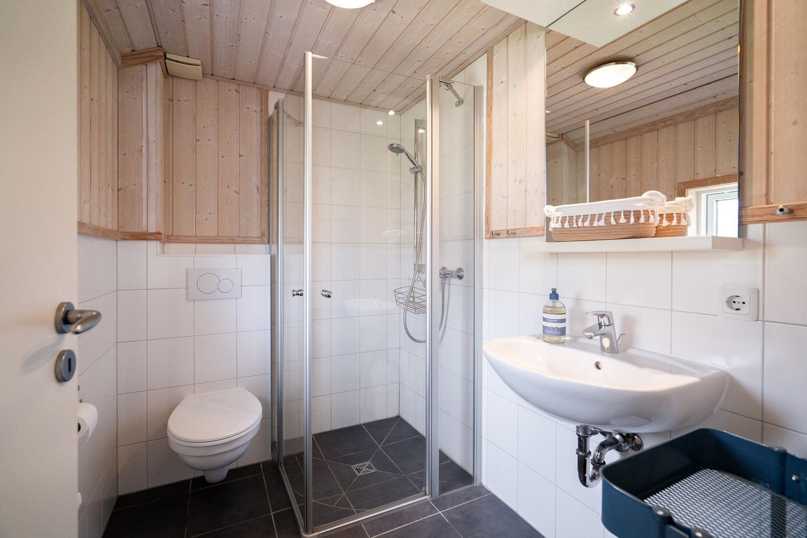 Badezimmer mit Dusche, Waschbecken und Toilette. Holzwände und Fliesen.