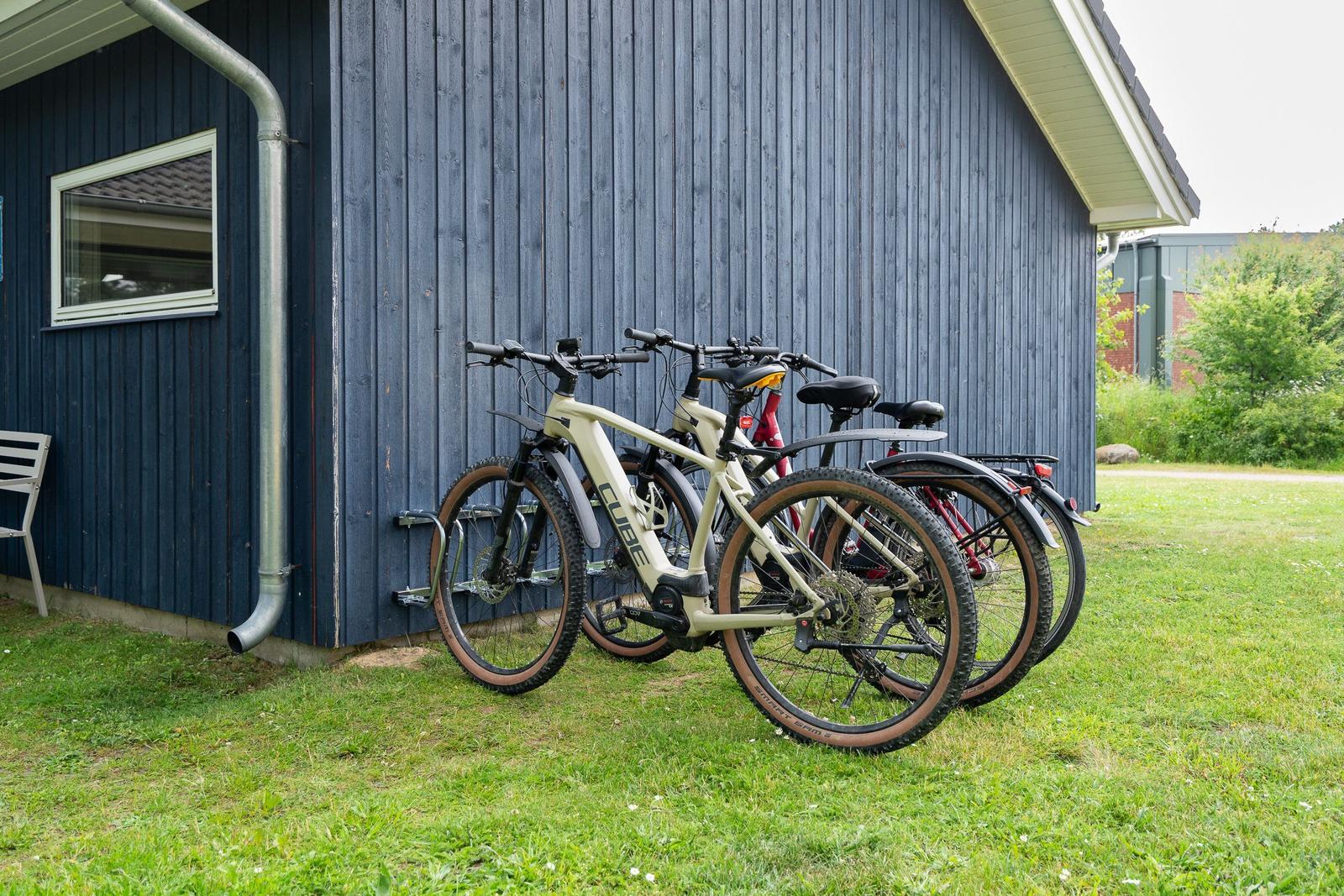Drei Fahrräder stehen vor einem blauen Holzhaus auf einer Wiese.