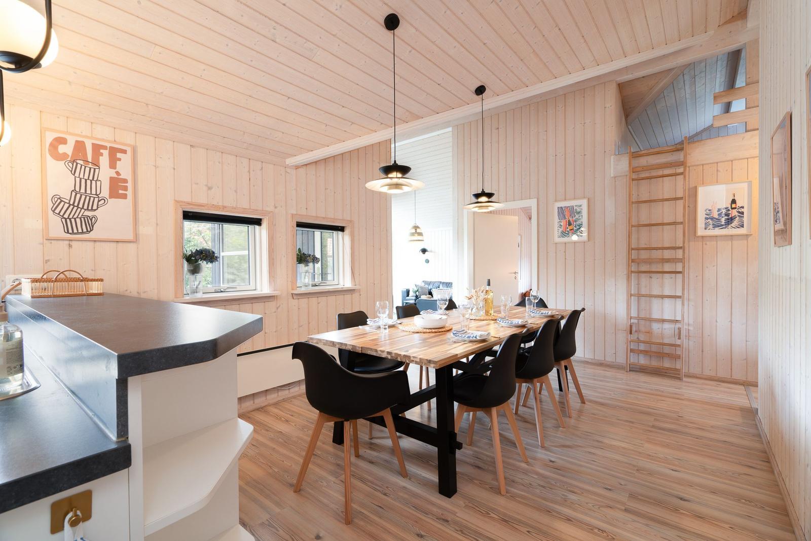 Esszimmer mit Holztisch, schwarzen Stühlen und Kücheninsel. Holzwände und Decke.