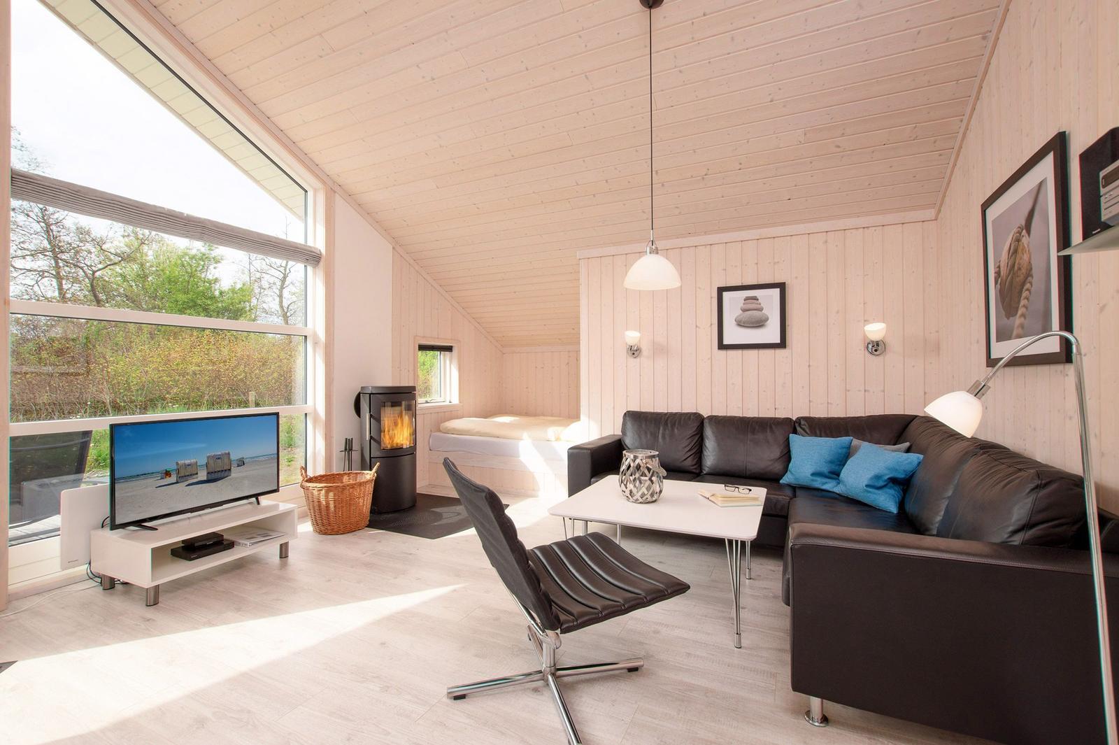 Wohnzimmer mit Sofa, Fernseher und Kamin. Große Fenster und Holzwände.
