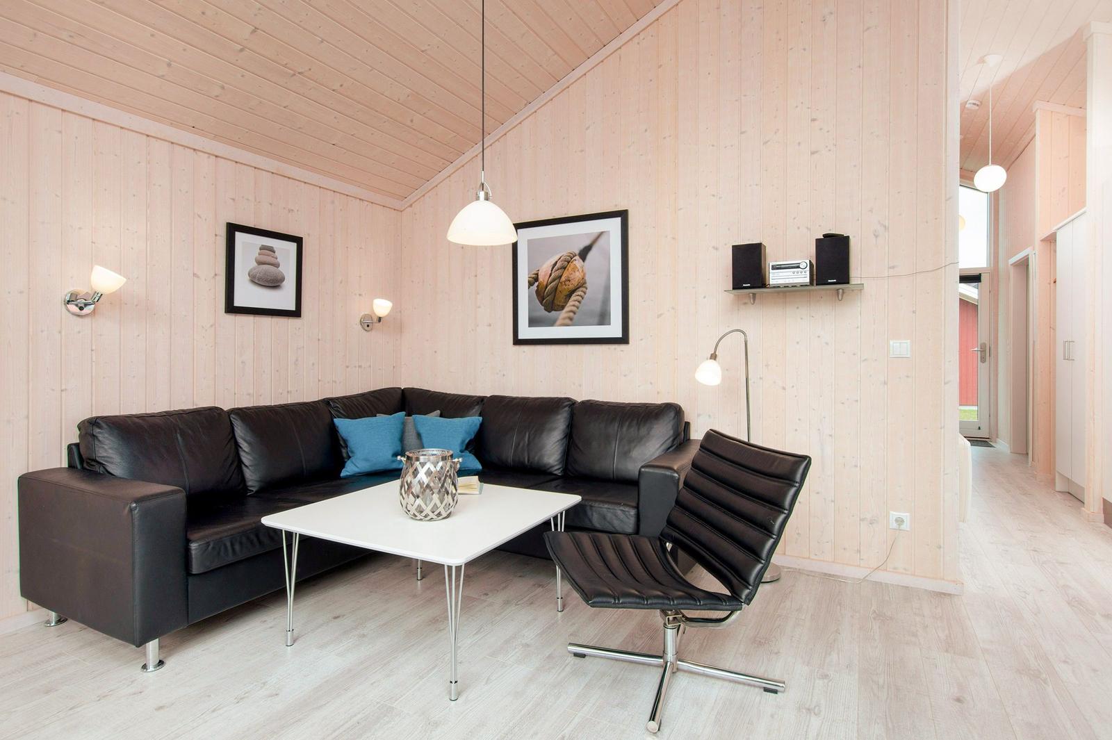 Wohnzimmer mit Ledersofa, Tisch und Stuhl. Holzwände und -decke. Wandlampen und Bilder.