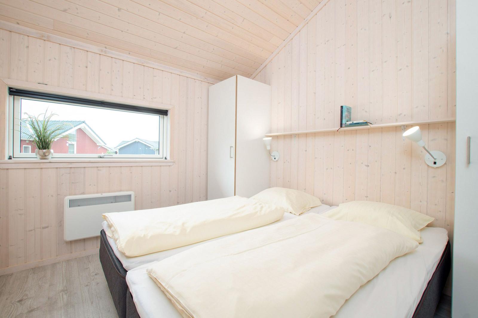 Schlafzimmer mit Bett, Fenster, Kleiderschrank und Wandregal.