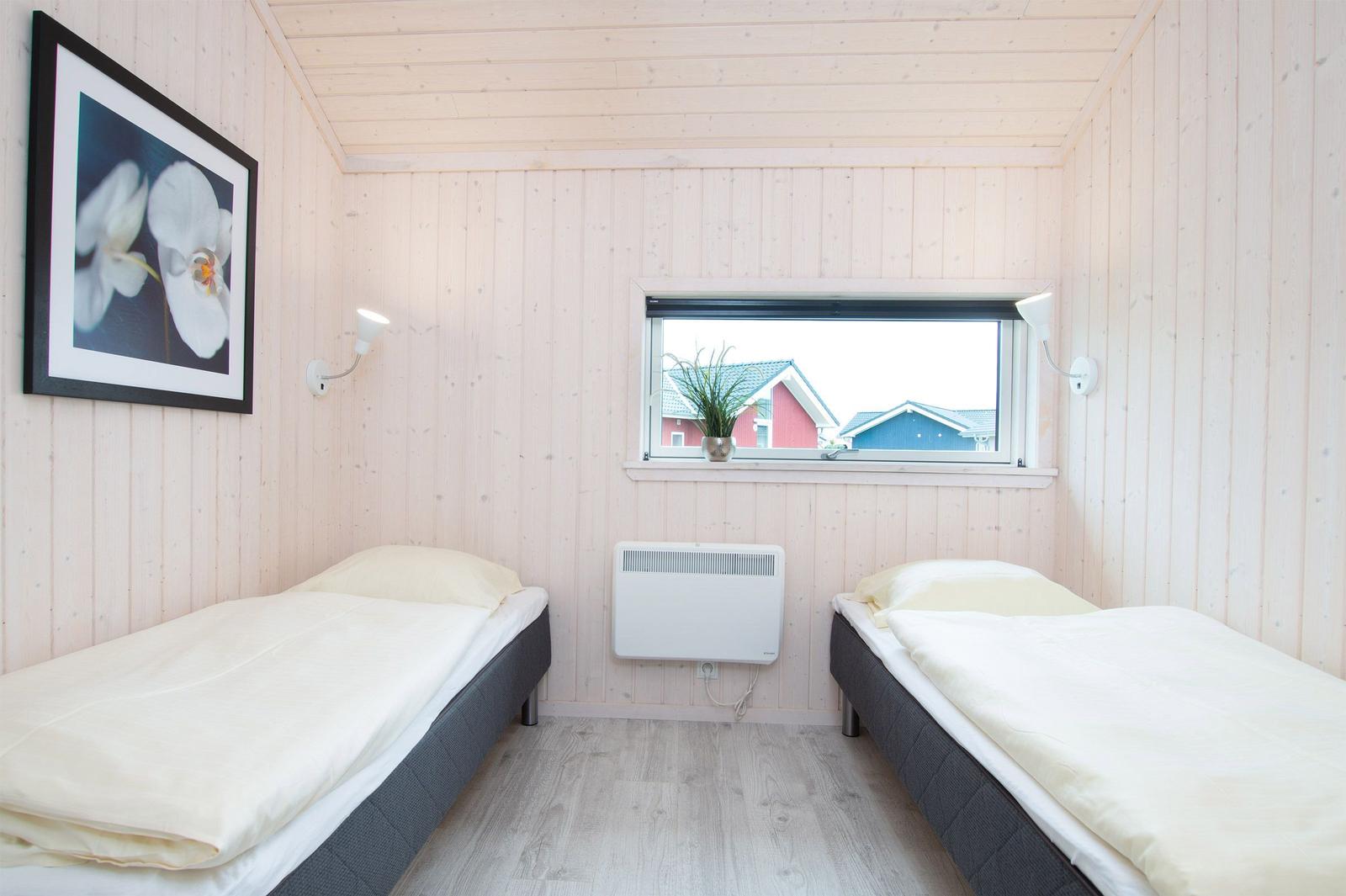 Zwei Einzelbetten in einem Raum mit Holzwandverkleidung und Fensterblick auf Häuser.