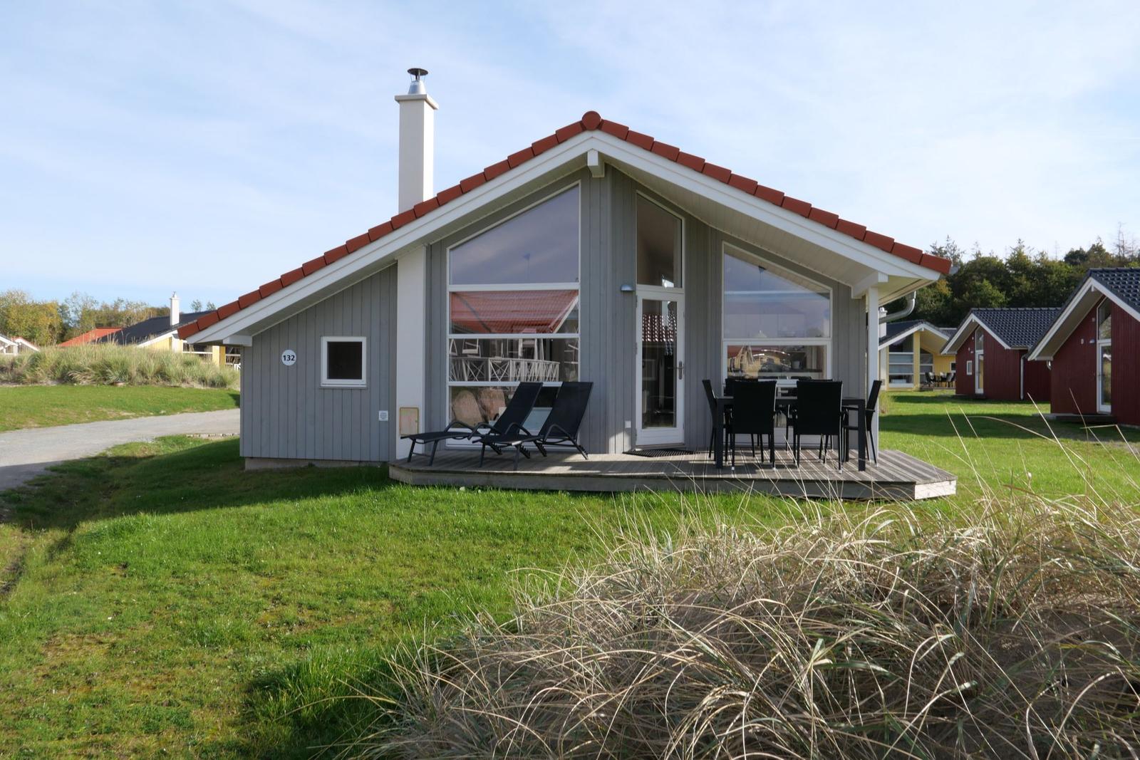 Moderne Holzhütte mit Terrasse, Garten und Sitzgelegenheiten.