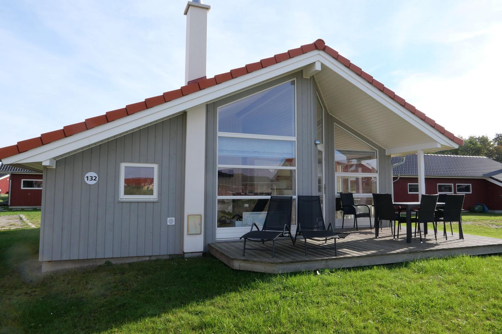Haus mit Terrasse, Sitzgelegenheiten und Garten. Hausnummer 132. Dach mit roten Ziegeln.