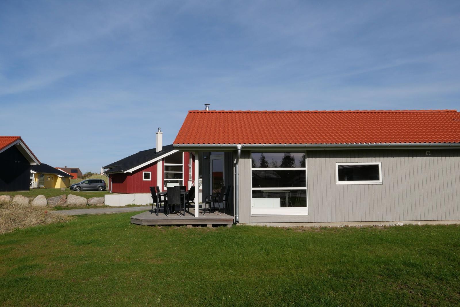 Ein Haus mit rotem Dach und Terrasse mit Tisch und Stühlen.
