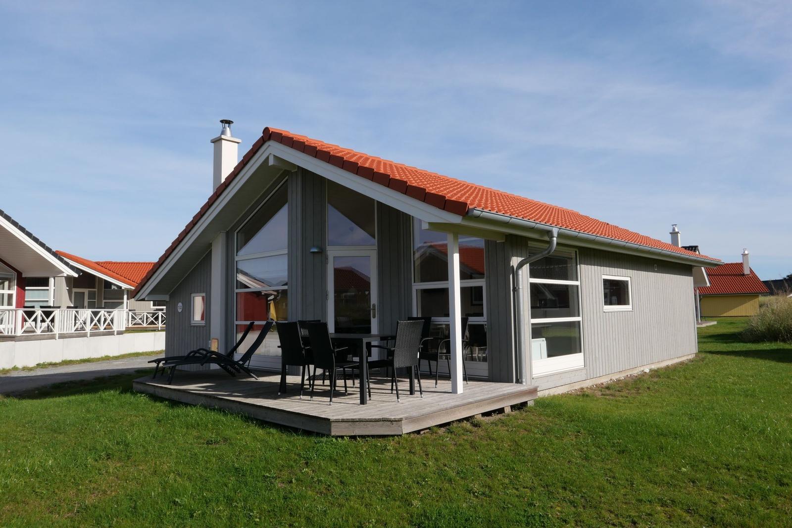 Moderne Villa mit Terrasse, Tisch und Stühlen, rotem Dach und grünem Rasen.