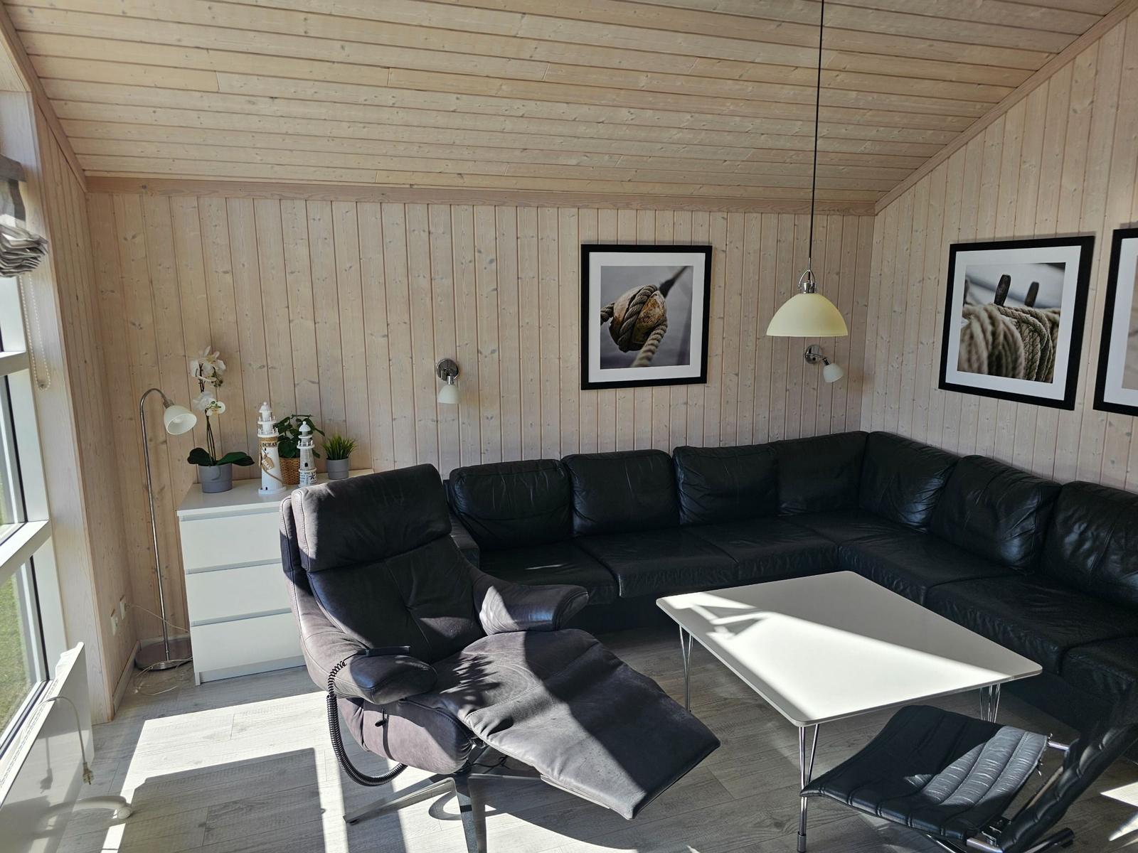 Wohnzimmer mit schwarzer Sofa-Ecke, schwarzem Sessel und weißem Tisch.