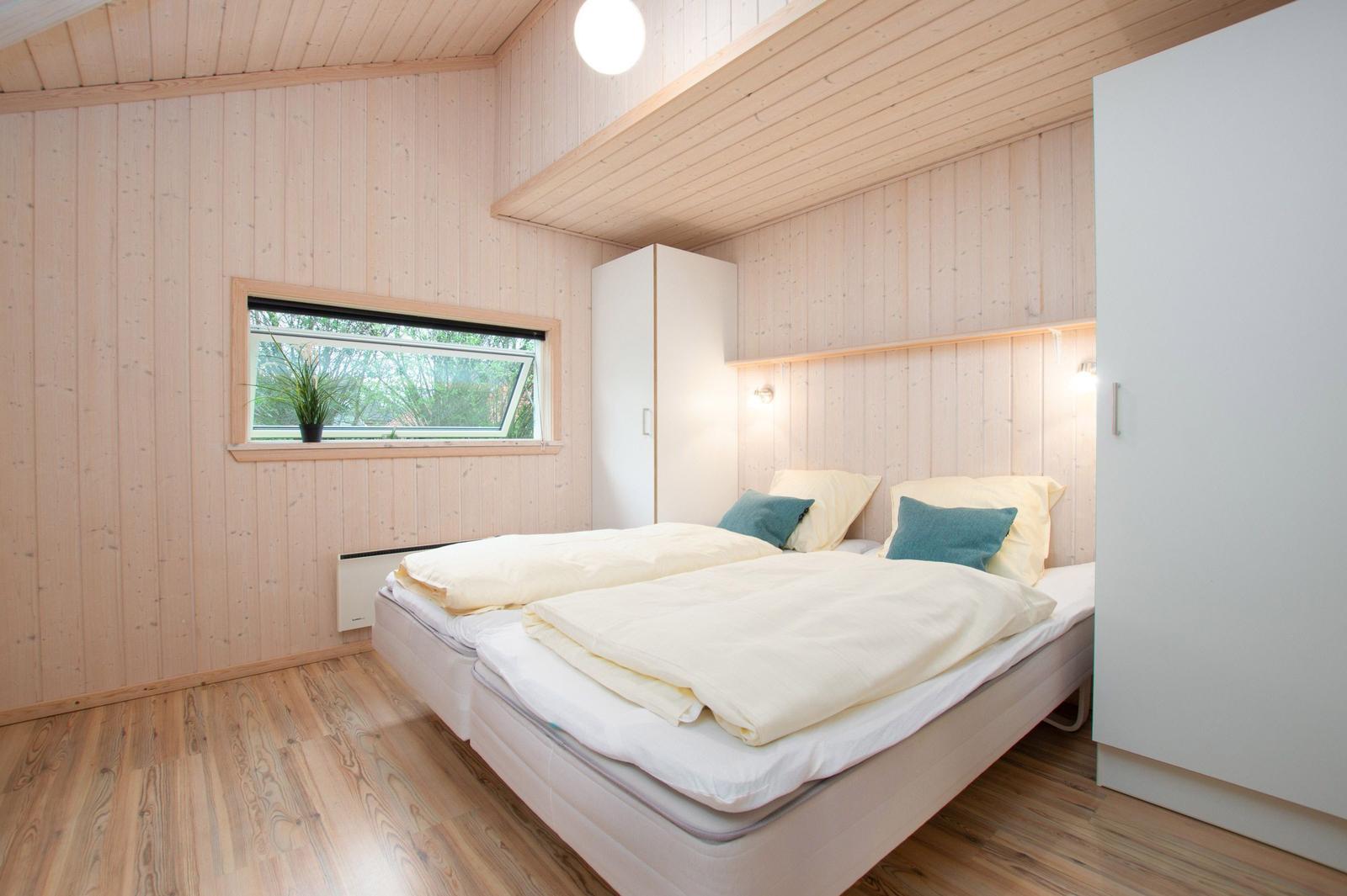 Schlafzimmer mit Doppelbett, Holzwand und Fenster. Weiße Schränke und Holzboden.