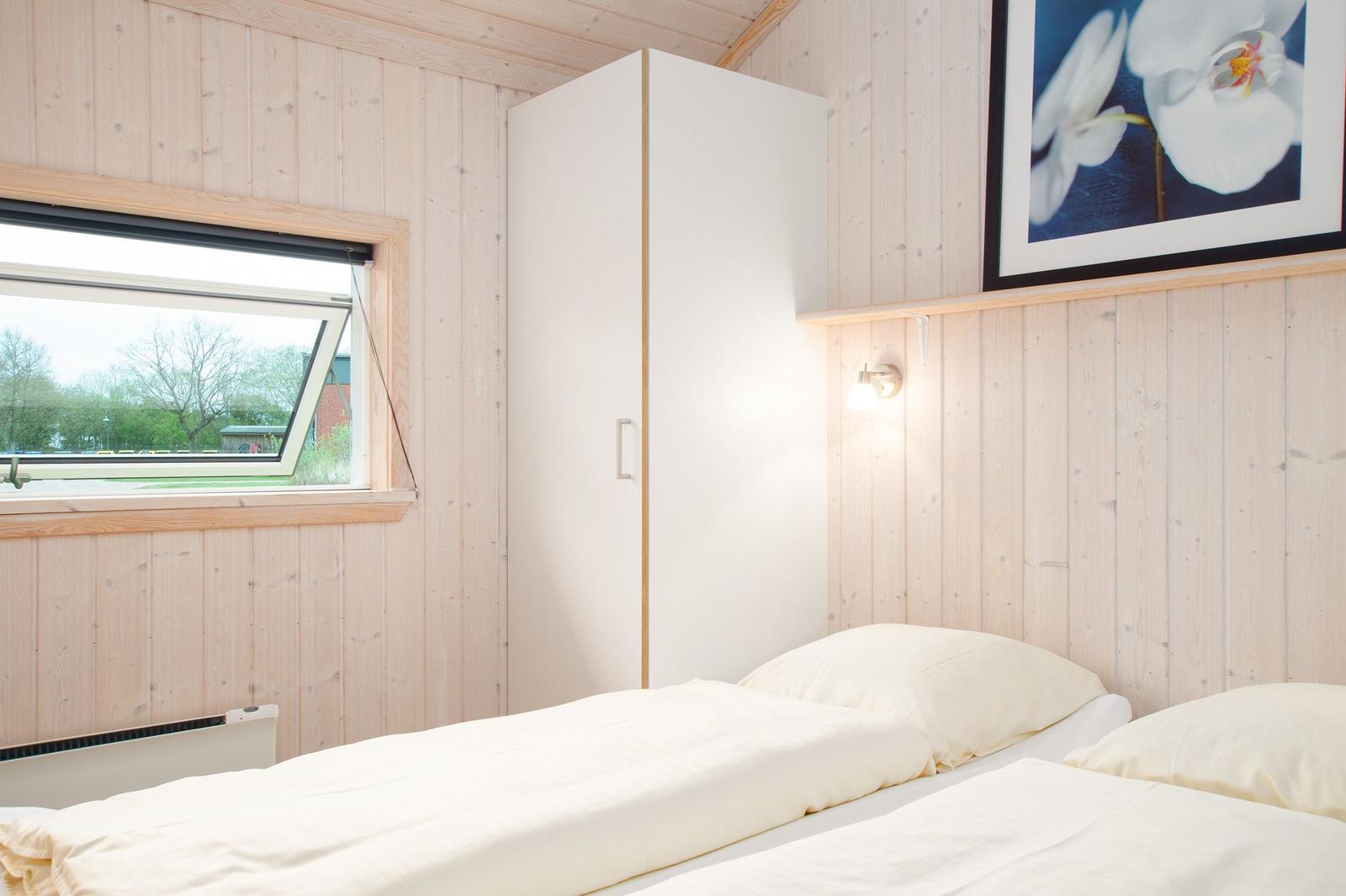 Schlafzimmer mit Bett, Kleiderschrank und Fenster. Holzwand und Blumenbild.