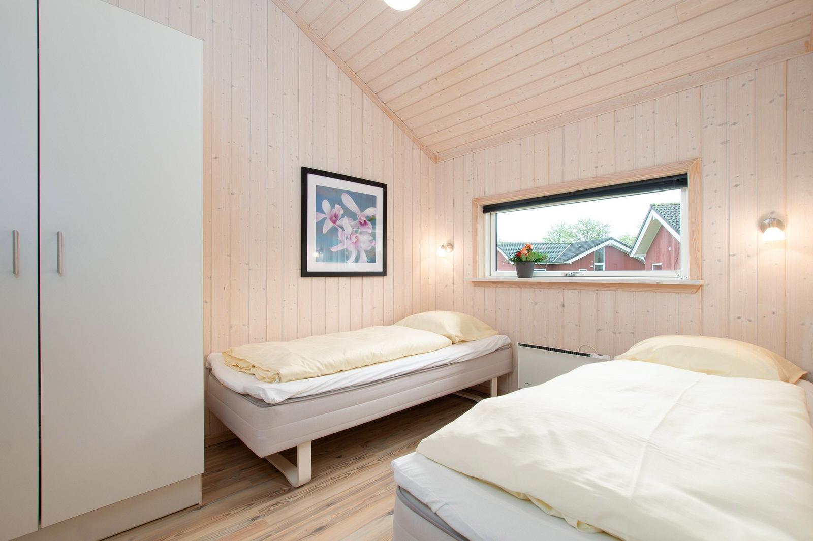 Zwei Betten in einem Raum mit Holzwandverkleidung und Fensterblick auf ein Haus.