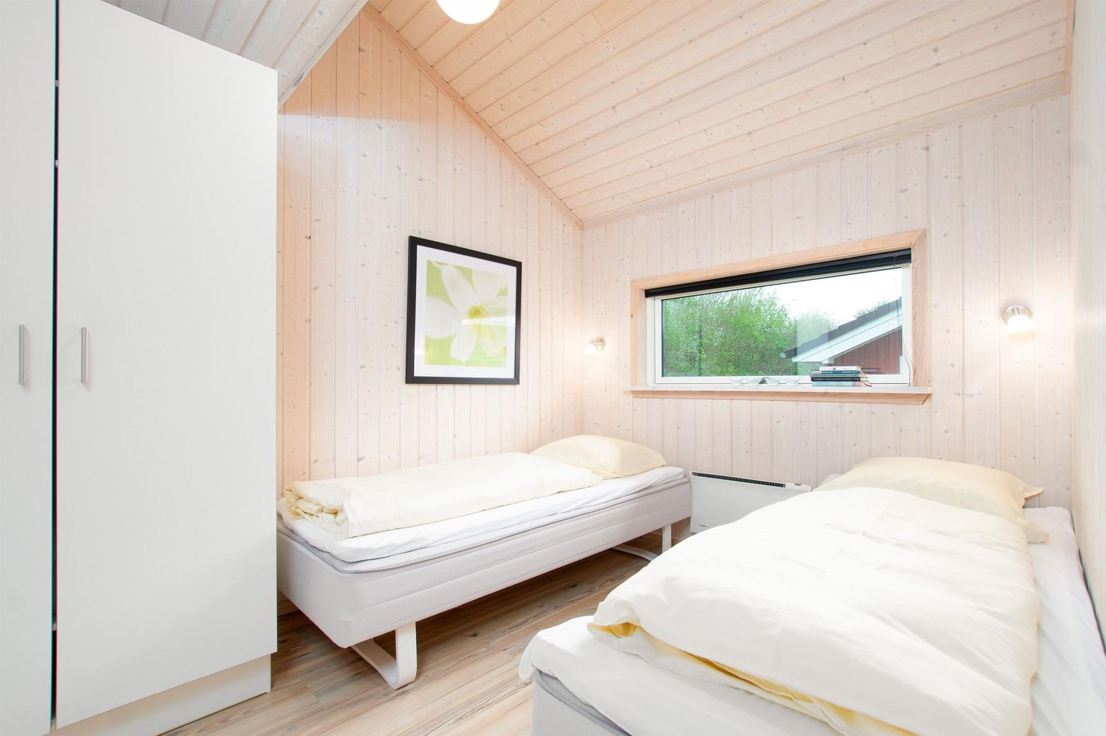 Zwei Betten, Schrank und Fenster in einem Holzhauszimmer.