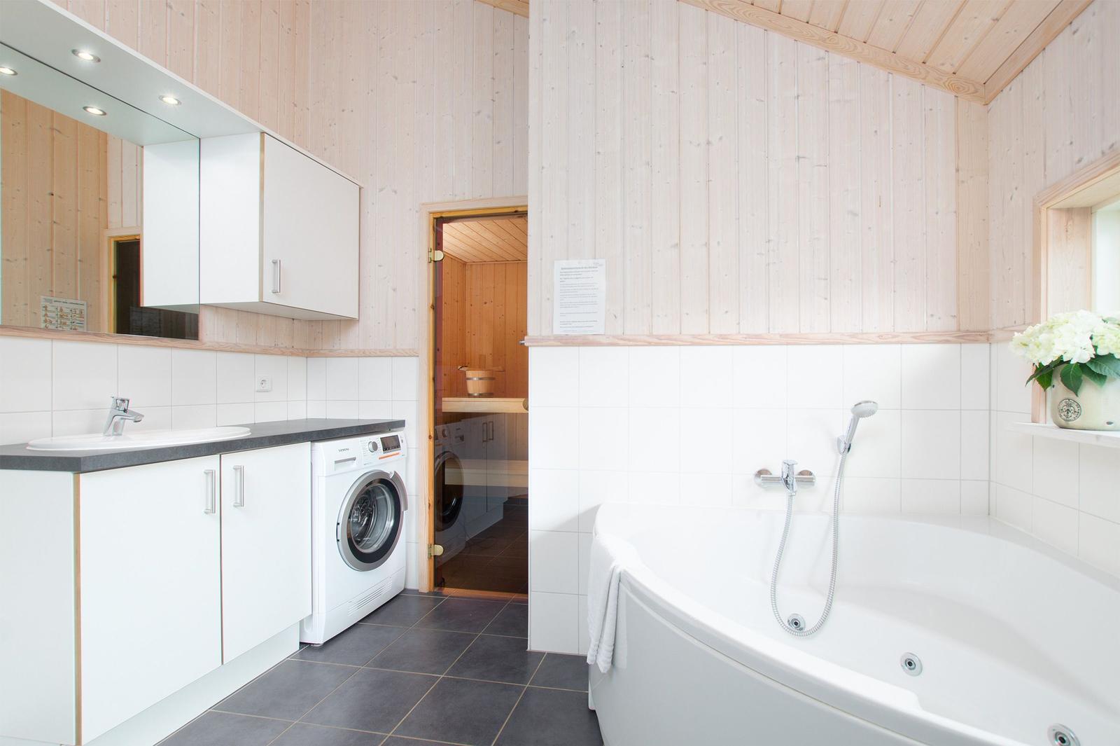 Badezimmer mit Badewanne, Waschmaschine und Dusche. Holzwände und Fliesen.
