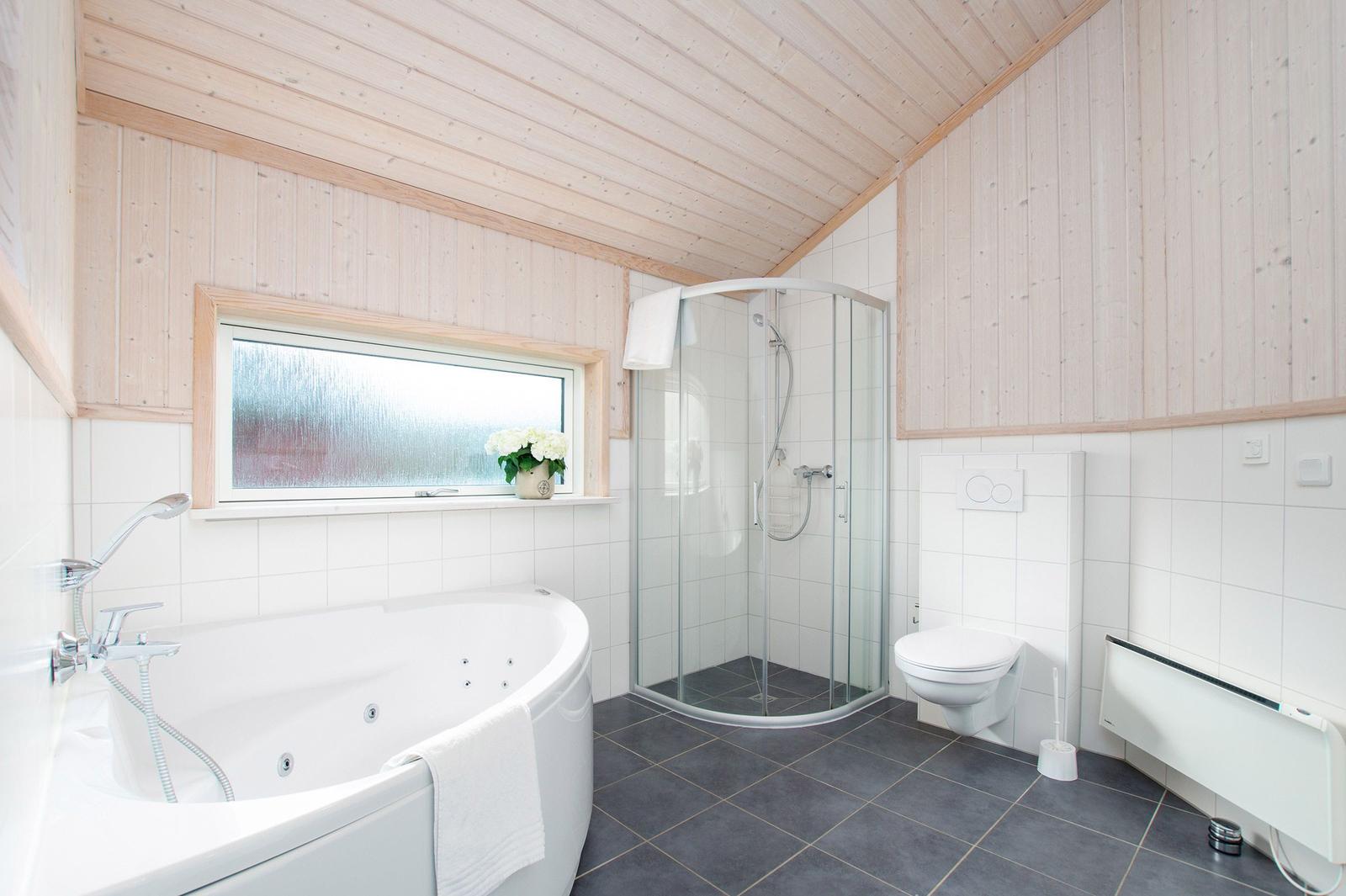 Badezimmer mit Whirlpool, Dusche und Toilette. Holzwände und Fenster mit Blumen.