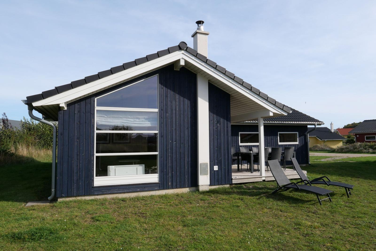 Ein blaues Ferienhaus mit Terrasse und Liegen im Gras.