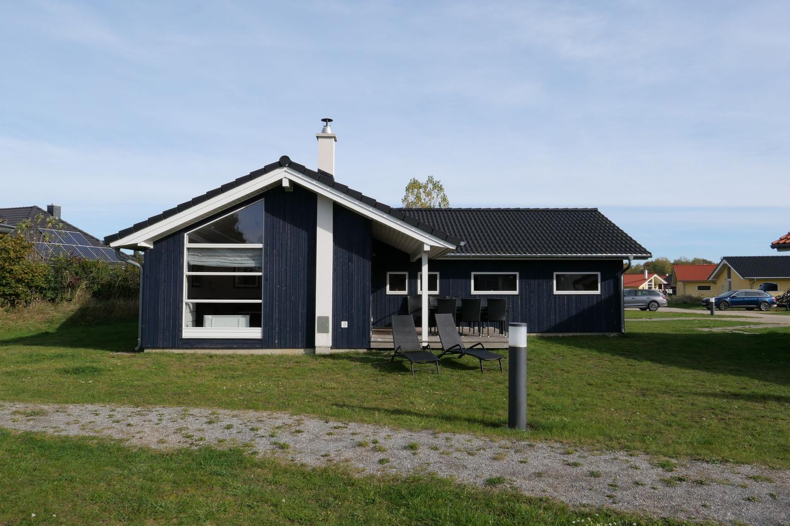 Ein blaues Haus mit Terrasse und Liegestühlen auf einer grünen Wiese.
