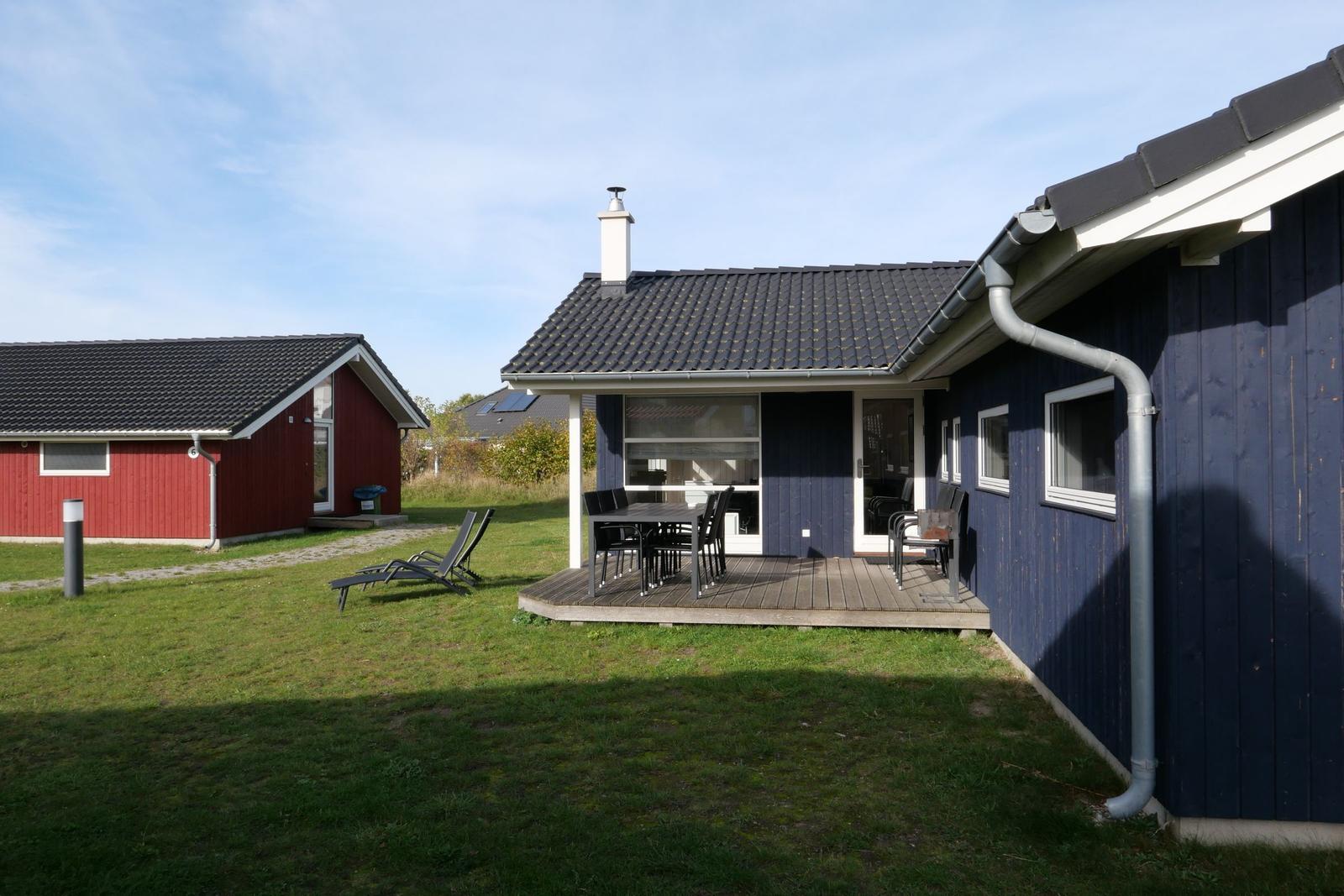 Blau gestrichenes Haus mit Terrasse, Garten und Liegestühlen. Nebenhaus rot.