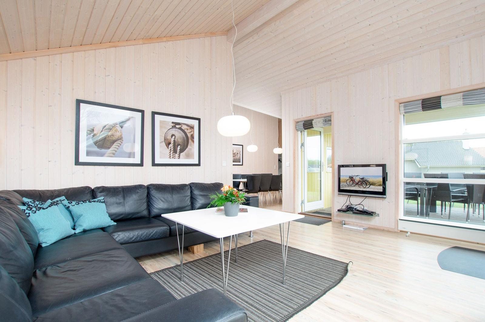 Wohnzimmer mit schwarzer Couch, weißem Tisch und Fernseher an der Wand.