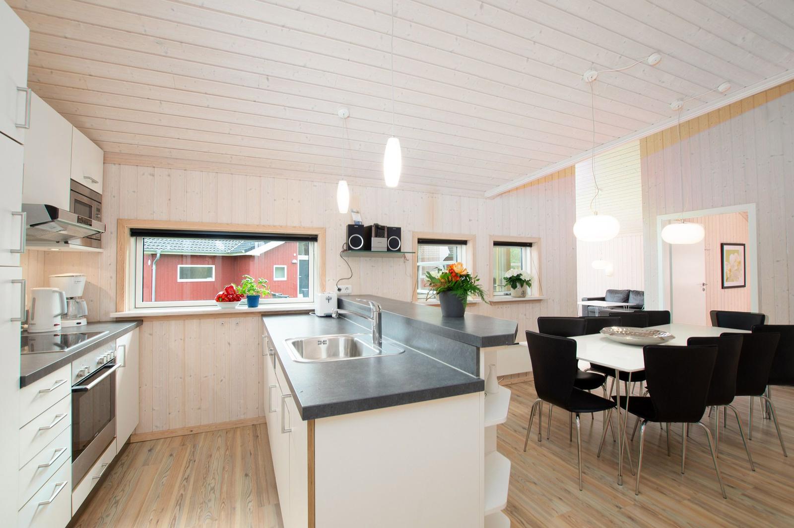 Küche mit Essbereich, Holzdecke und -wände, schwarze Arbeitsplatten, weiße Schränke und schwarze Stühle.