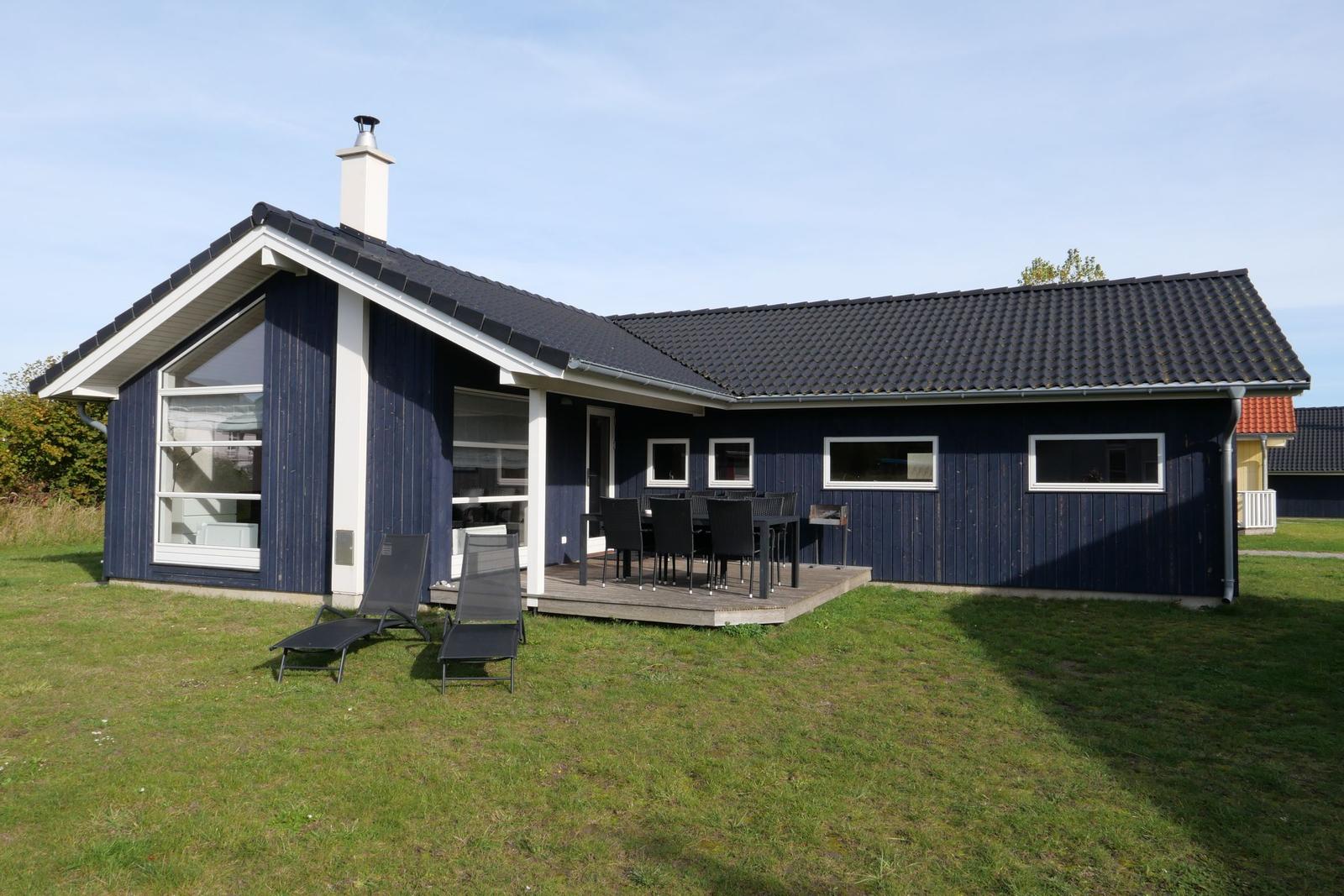 Ein blaues Ferienhaus mit Terrasse und Liegestühlen auf einer grünen Wiese.