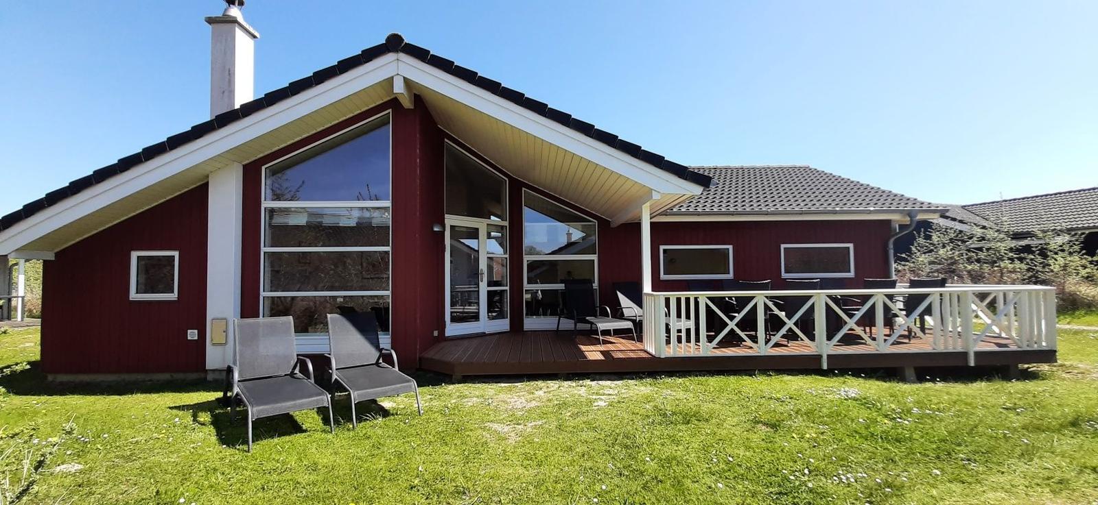 Rotes Haus mit Terrasse und Garten. Große Fenster und Holzveranda.