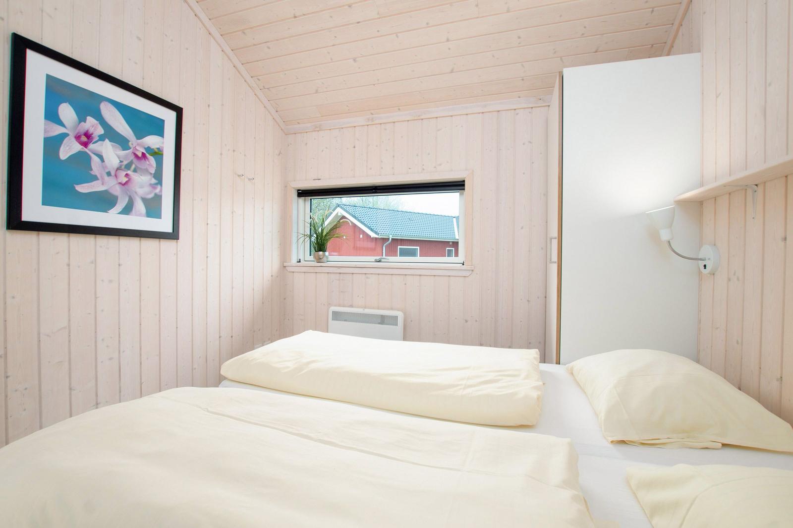 Schlafzimmer mit Bett, Wandbild und Fensterblick auf rotes Haus.