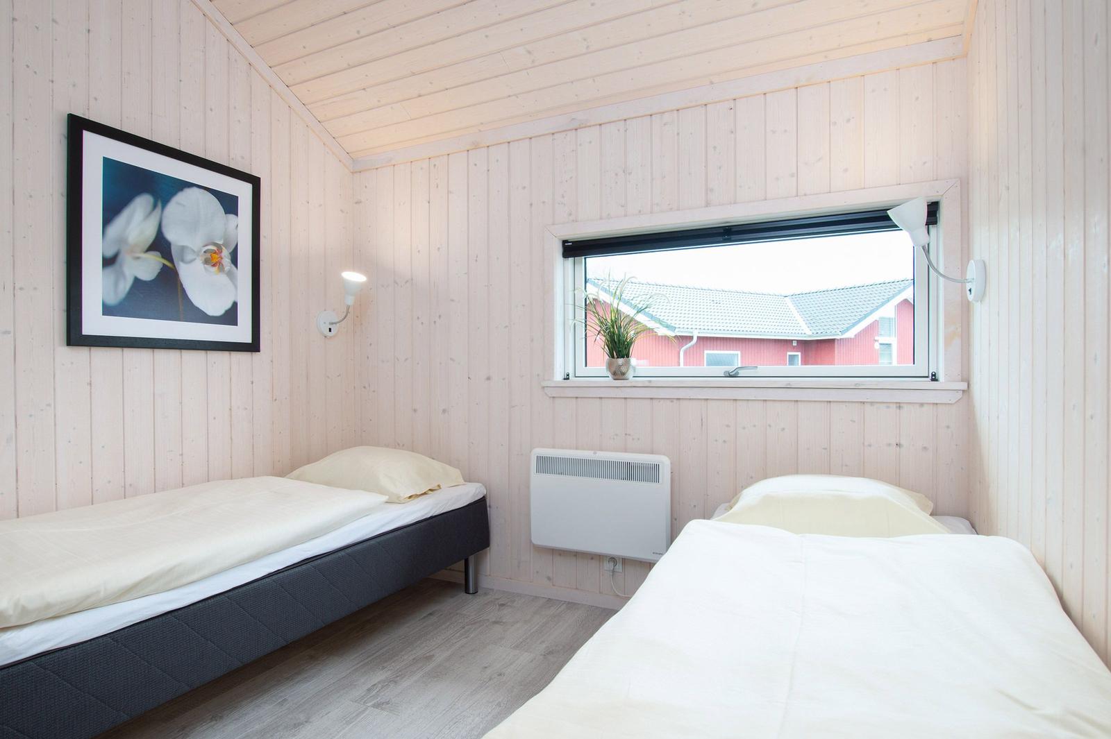 Zwei Betten in einem Raum mit Holzwänden und Fensterblick auf ein rotes Haus.