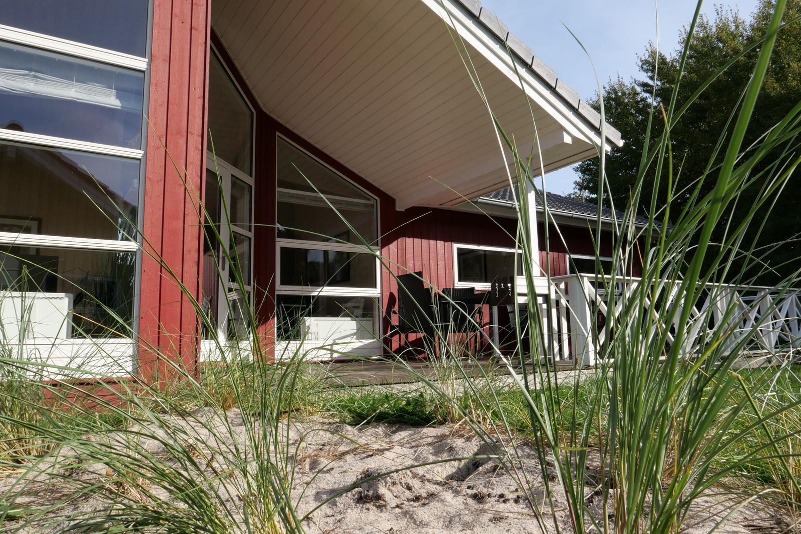 Rotes Haus mit großem Fenster und Terrasse im Sand mit Gräsern