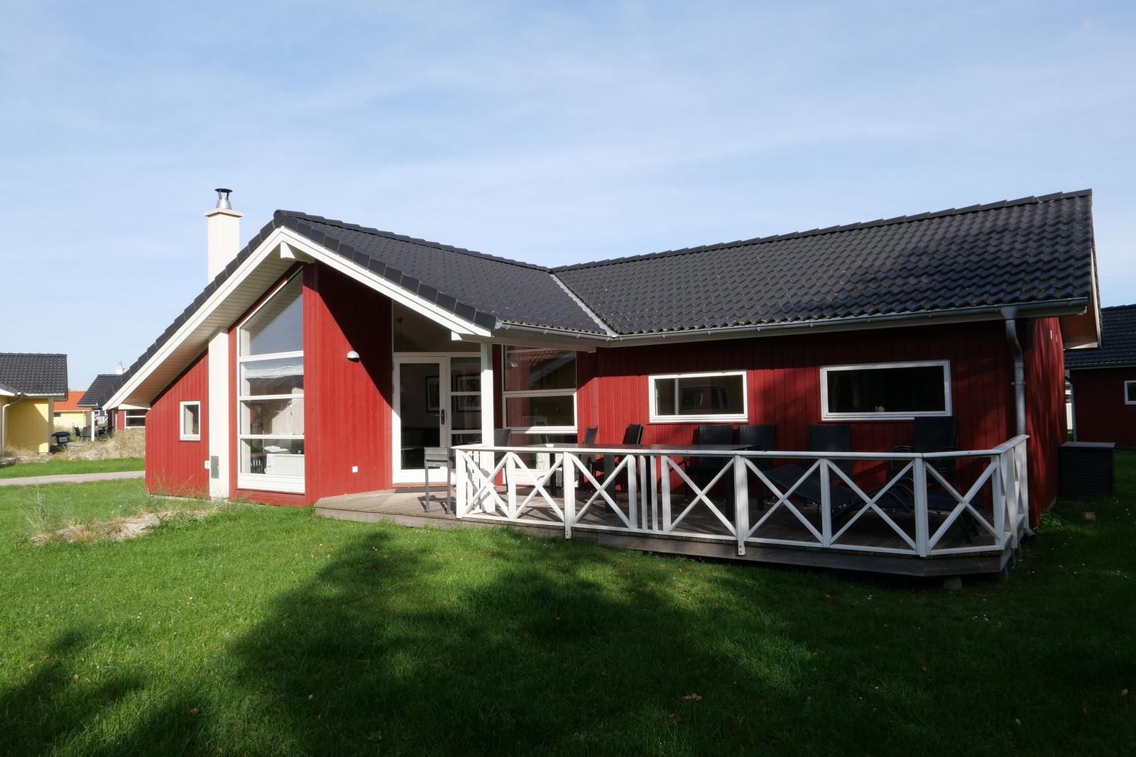 Rotes Ferienhaus mit Terrasse und Garten. Schwarzer Dachfirst und weiße Veranda.