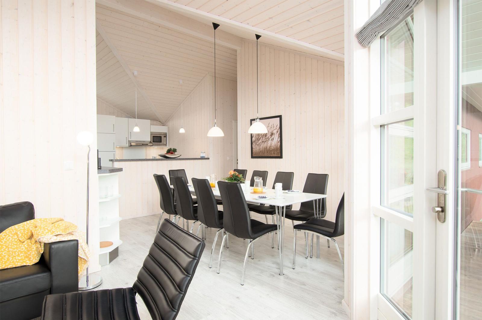 Essbereich mit Tisch und Stühlen, Küche und Wohnbereich mit Holzwänden und Fenster.