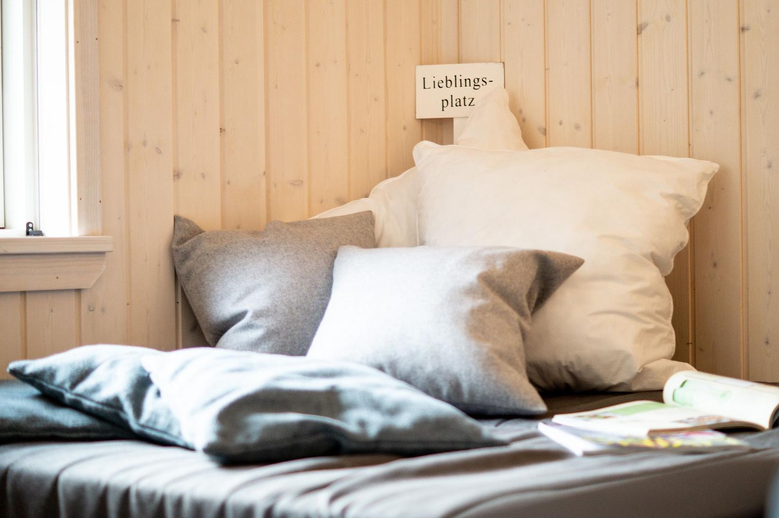 Ein Bett mit Kissen und einer Zeitschrift neben einem Fenster an Holzwand mit Schild.