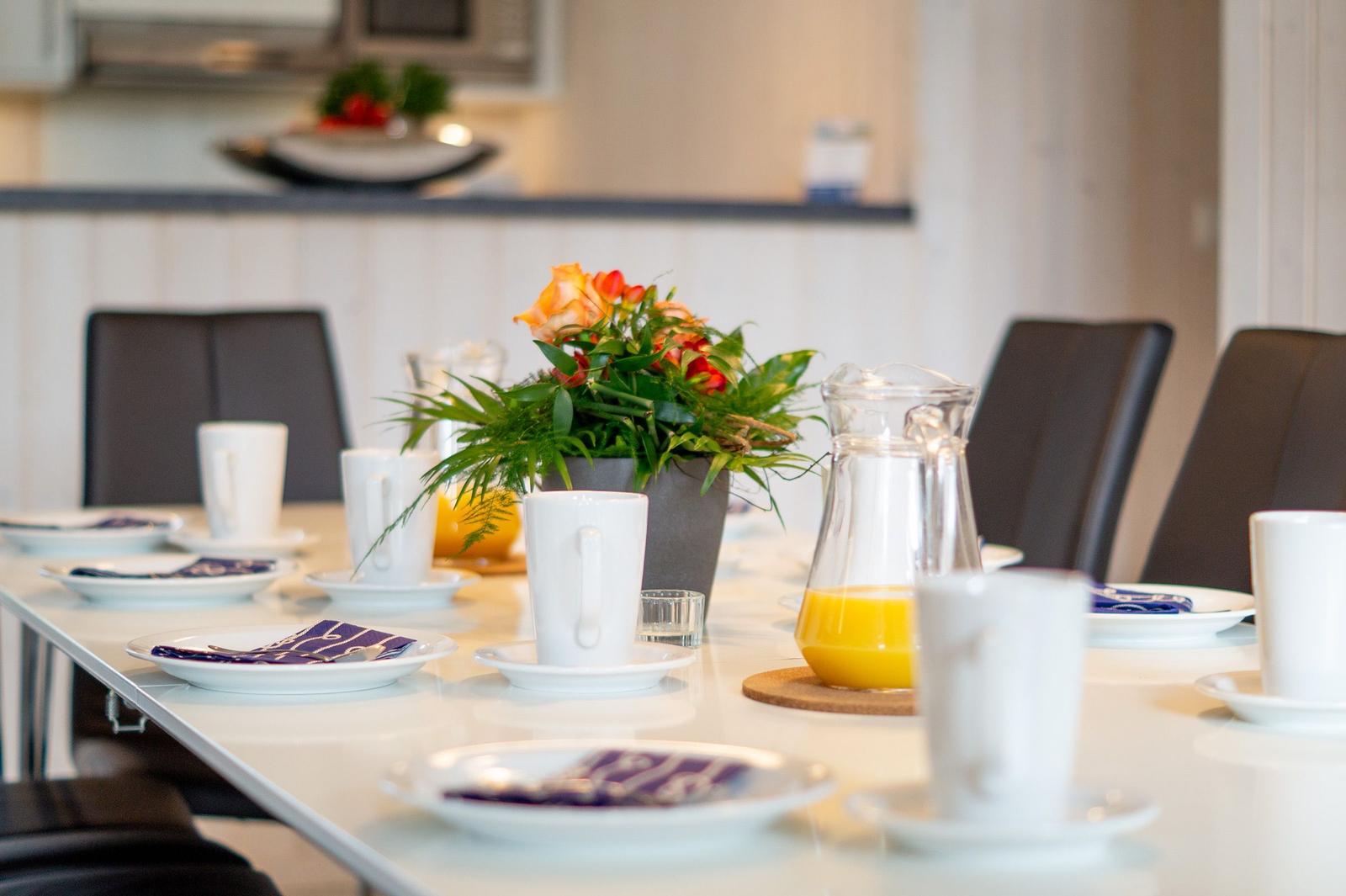 Esstisch mit Tassen, Tellern und einer Blumenvase.