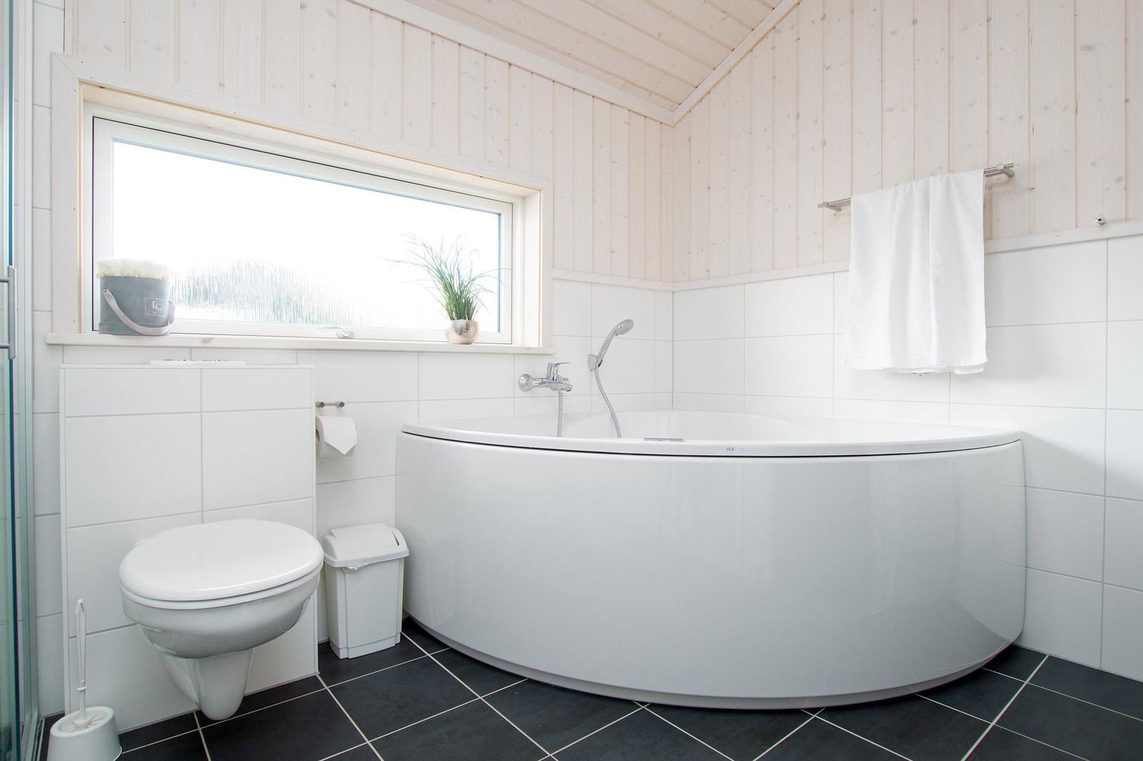 Badezimmer mit Badewanne, Toilette und Fenster. Holzwände und Fliesenboden.