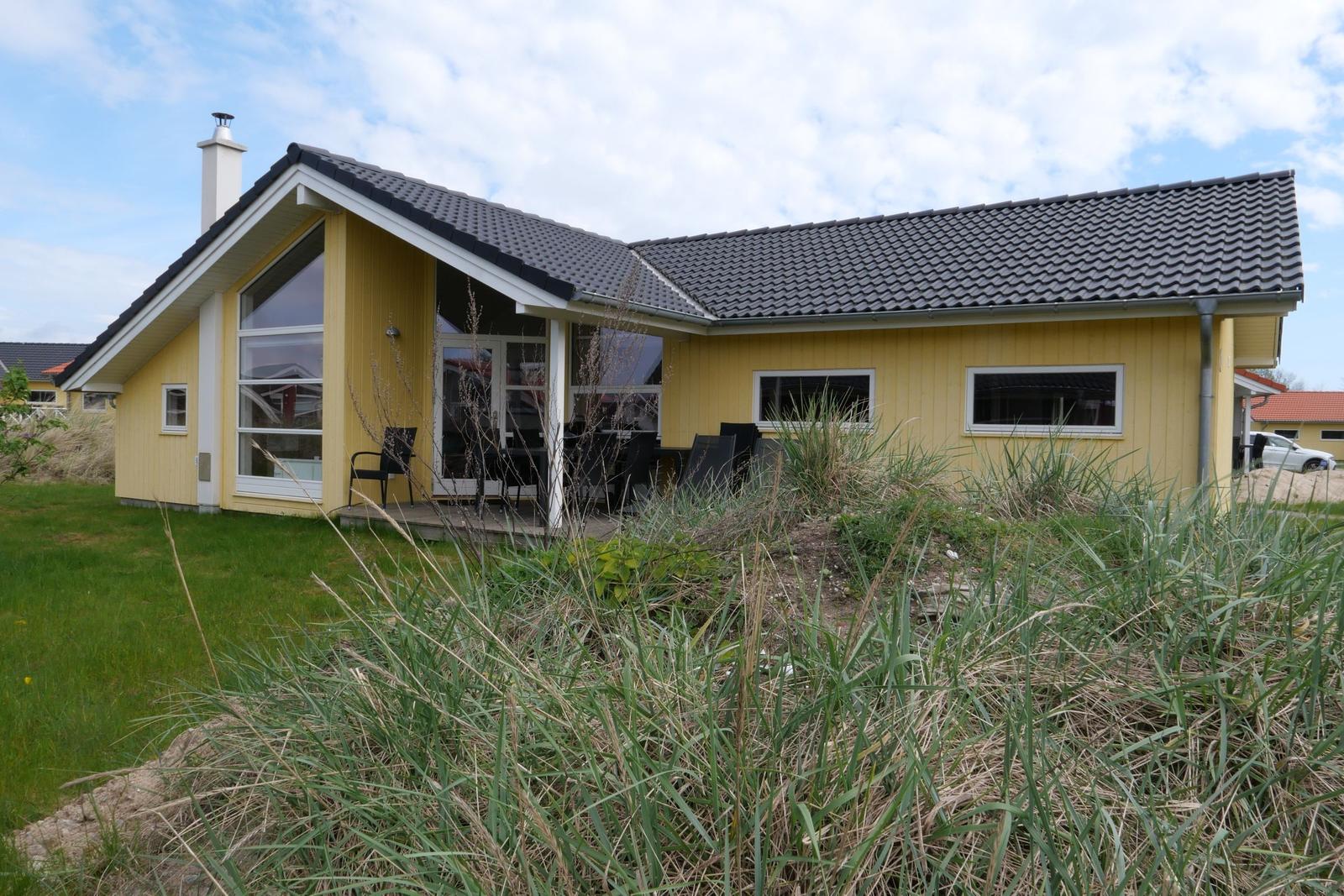 Ein gelbes Haus mit dunklem Dach und Terrasse im Vordergrund.
