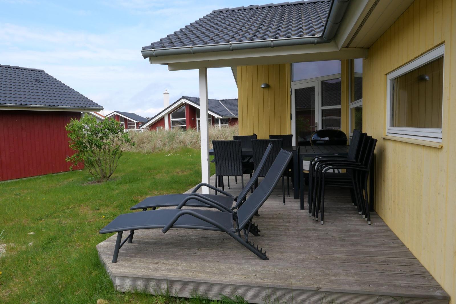 Terrasse mit Liegestühlen und Tisch. Gelbes Haus mit Sicht auf Gras und andere Häuser.